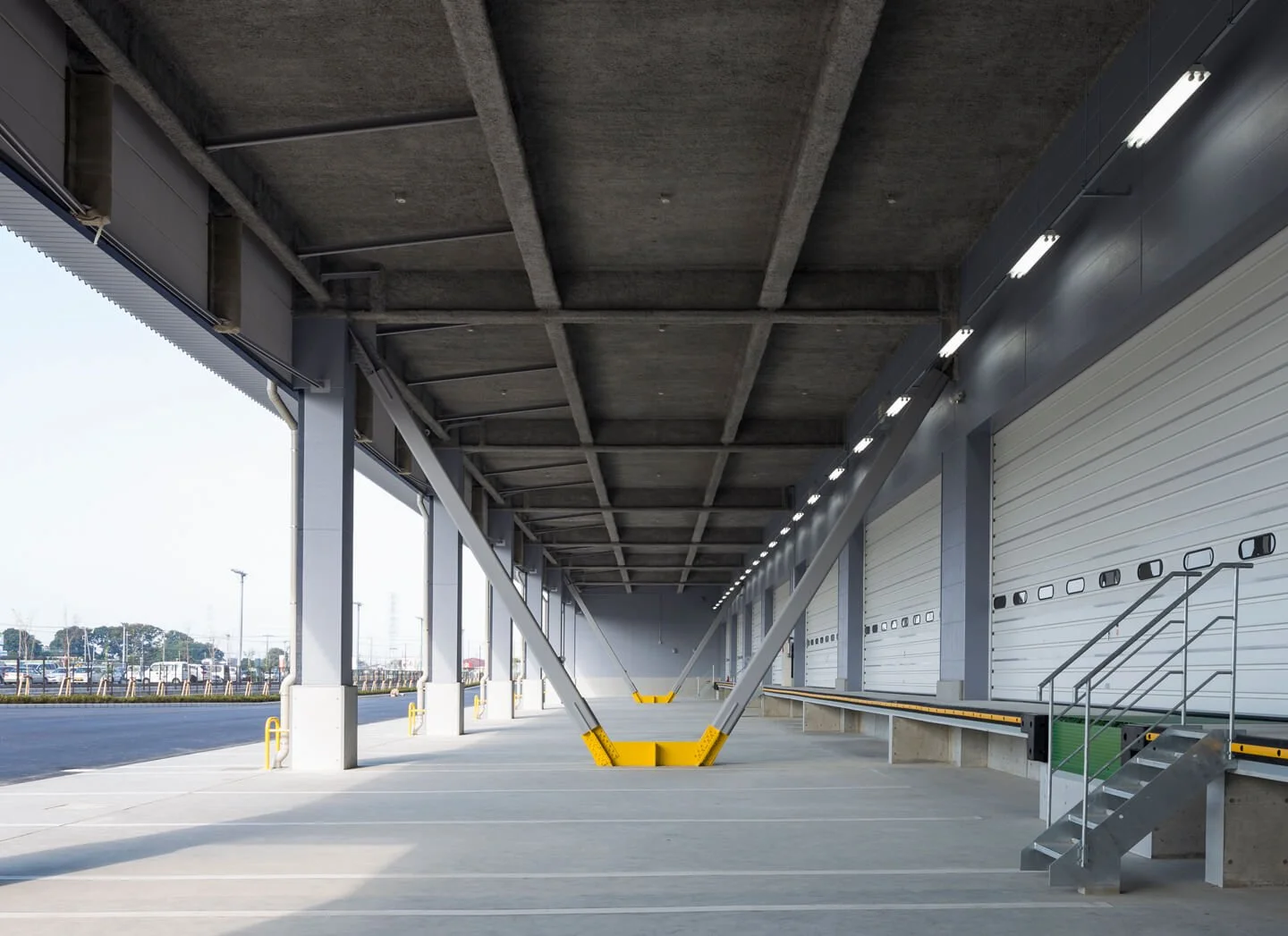 Empty warehouse loading dock with large rolling doors, concrete floor, and steel support beams.