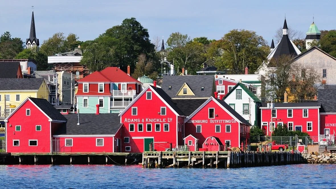 Colorful buildings along a waterfront with trees and church steeples in the background.