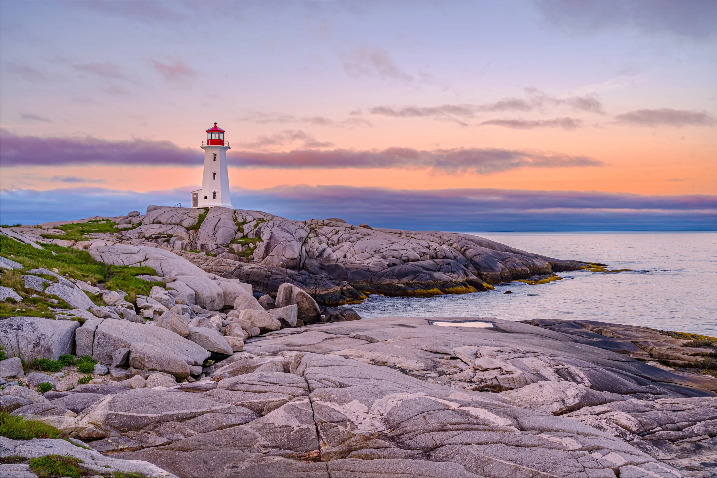A lighthouse on rocky coastline during sunset with colorful sky and calm ocean