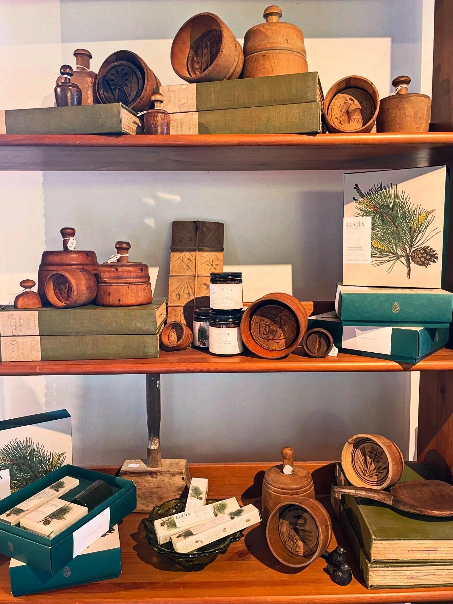 Wooden and cardboard merchandise on wooden shelves, including carved wooden containers, boxes, and jars, with some products labeled and packaged, suggesting a gift or home decor display.