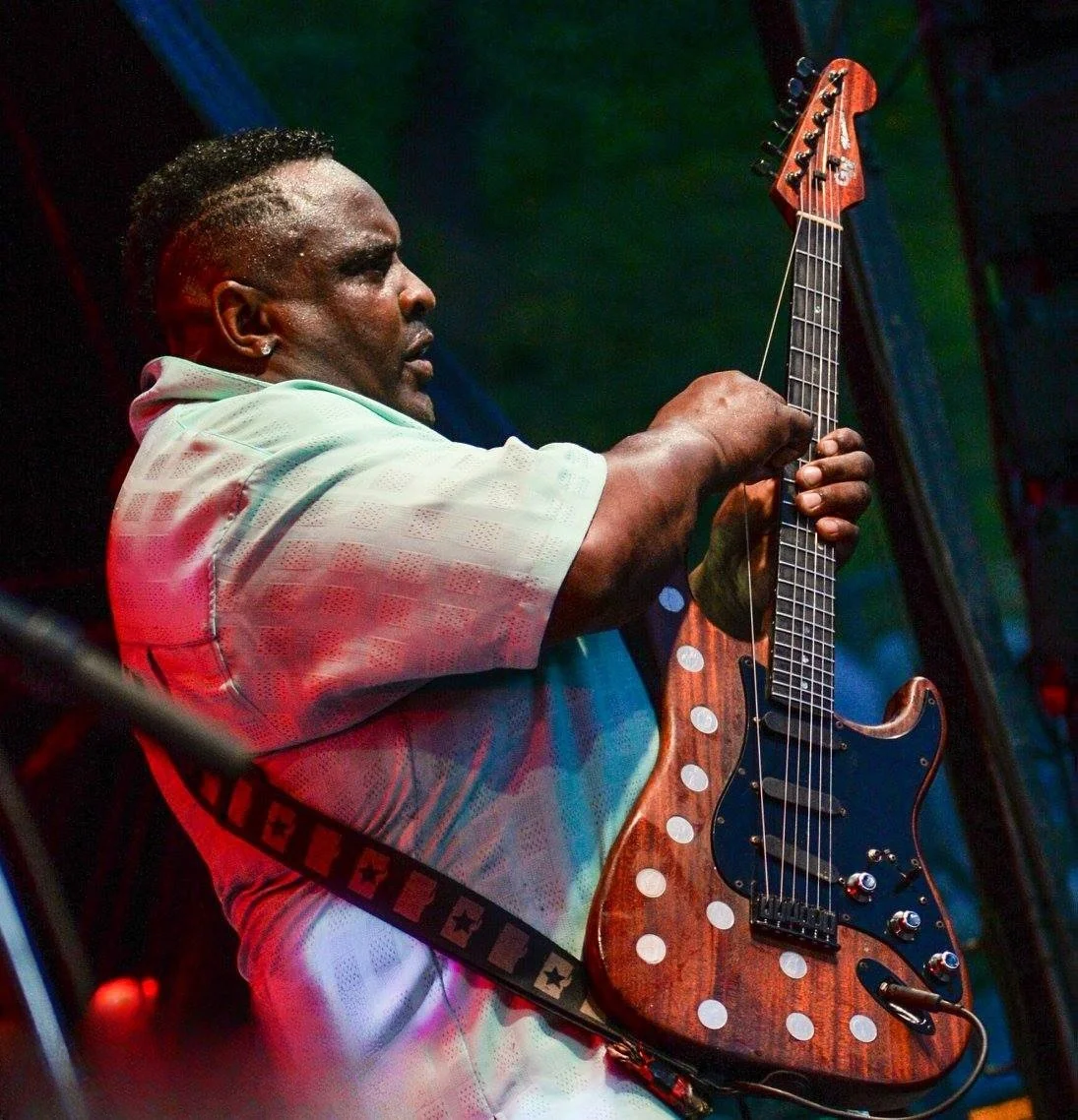A man playing an electric guitar on stage with colorful lighting.