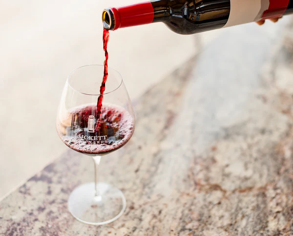 Person pouring red wine into a glass on a marble surface.