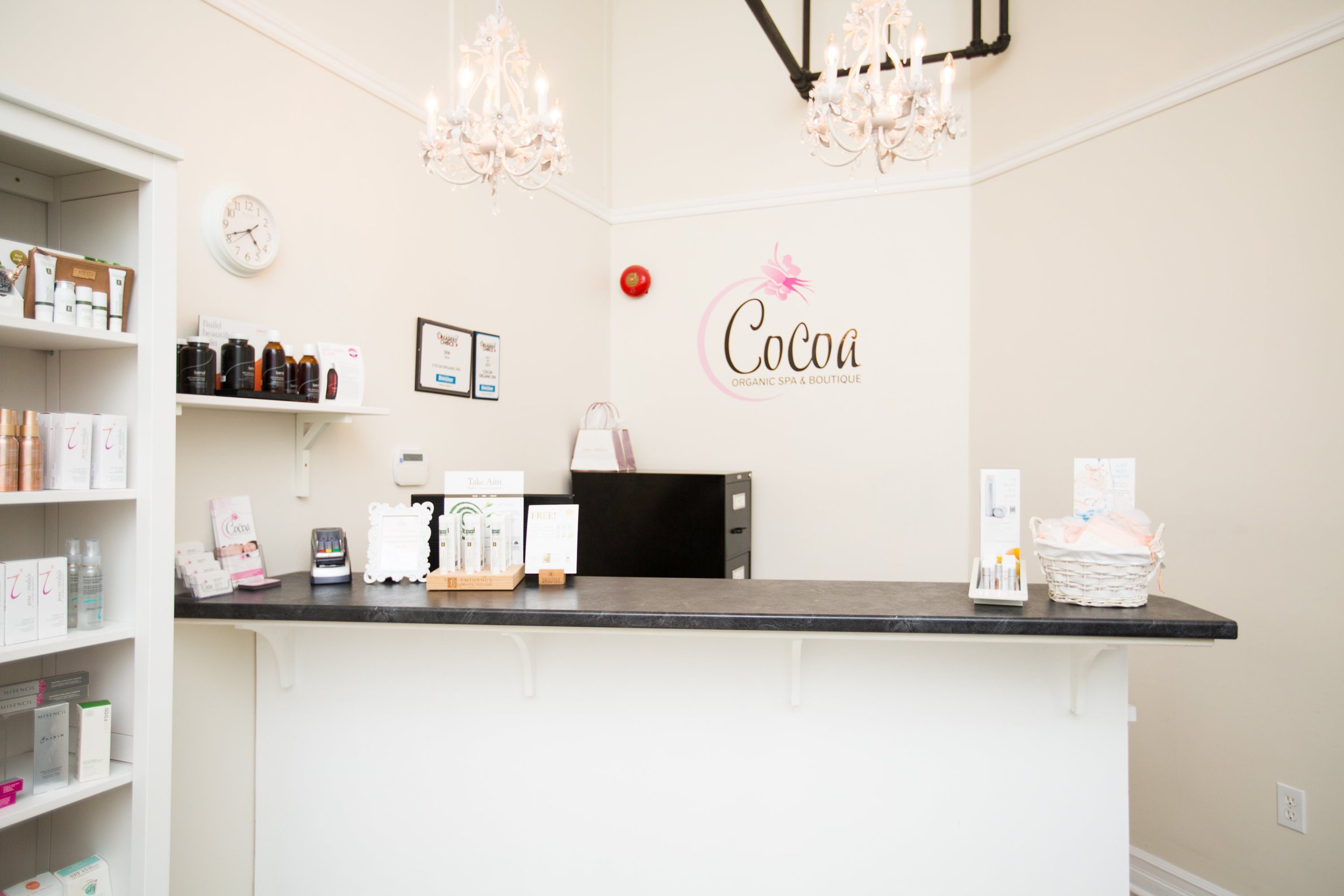 Reception area of Cocoa Organic Spa & Boutique with a black countertop, skincare products on the shelves, and a logo on the wall behind the counter.