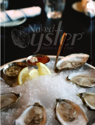 Fresh oysters on a bed of crushed ice with lemon wedges, accompanied by cocktail sauce and lemon slices, at The Naked Oyster bistro and bar.