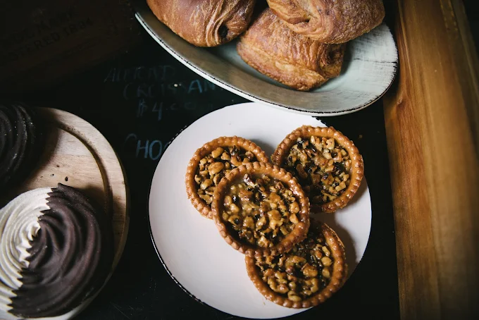 Assorted pastries on display including caramel pecan tarts, croissants, and a chocolate cupcake.