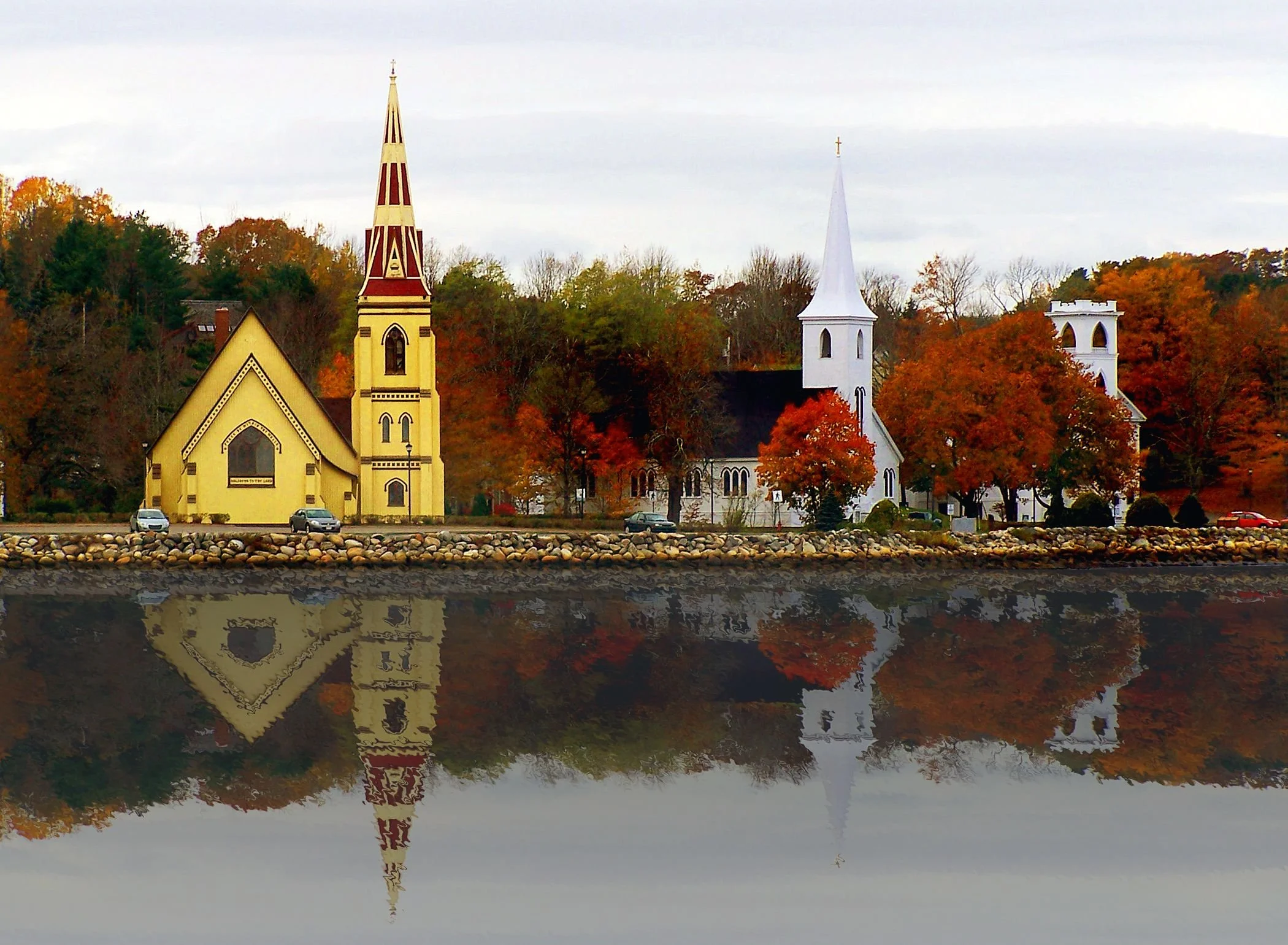 Scenic view of a colorful autumn landscape with two churches and their reflections in the calm water in the foreground.