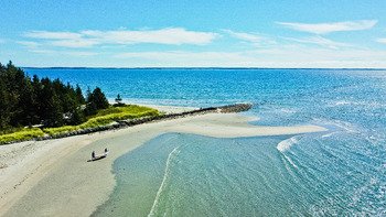 A beach with a sandy shoreline, a small boat on the sand, and a clear blue sky with some clouds.