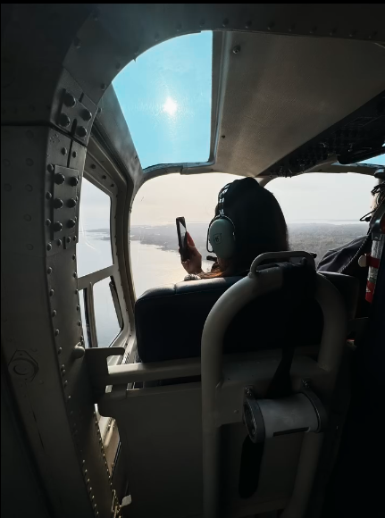 Passenger in aircraft cockpit taking a photo through the window with a smartphone, wearing headphones.