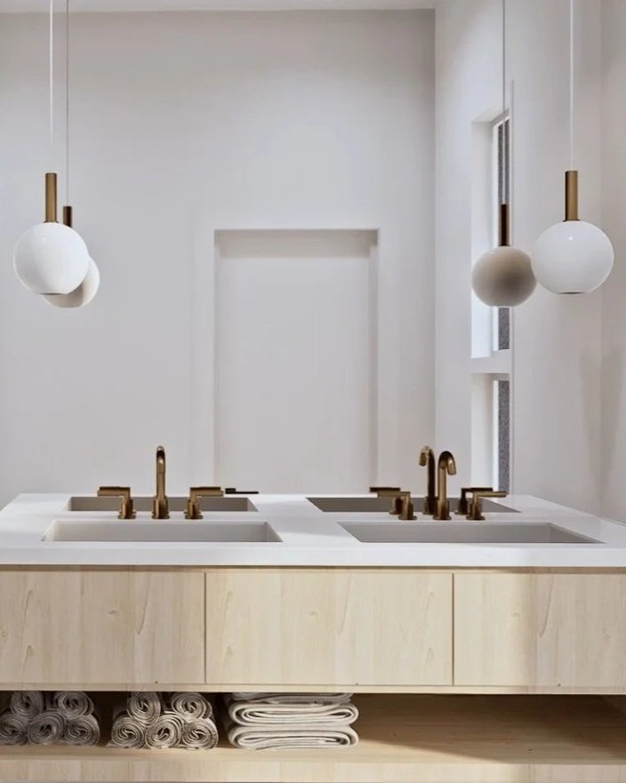 Modern bathroom with a double sink vanity, brass faucets, white countertops, and pendant lights with white globe shades.