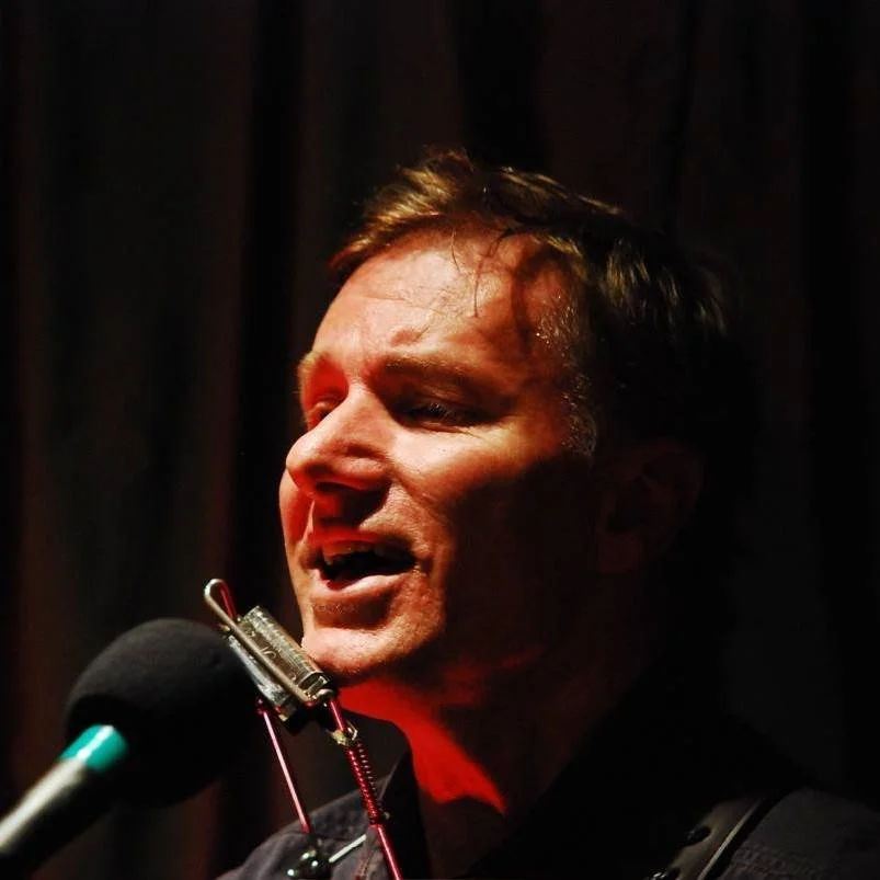 A man performing with a microphone in front of a dark background, singing passionately.