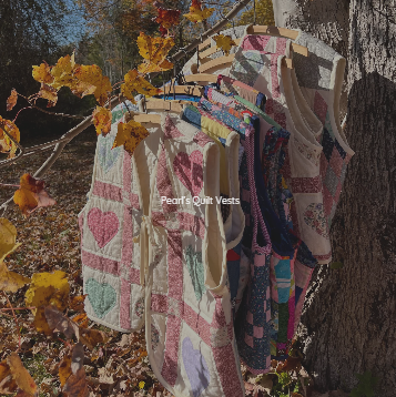Set of colorful quilt vests hanging on a clothesline outdoors among fall leaves.