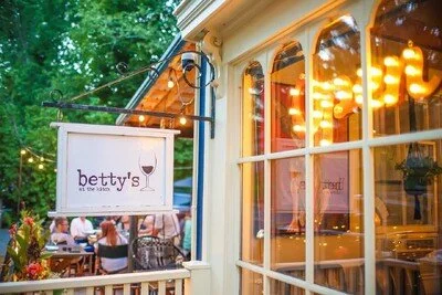 Outdoor view of Betty's restaurant with a hanging sign, string lights, and diners seated outside on a patio, with a bright and cozy ambiance.