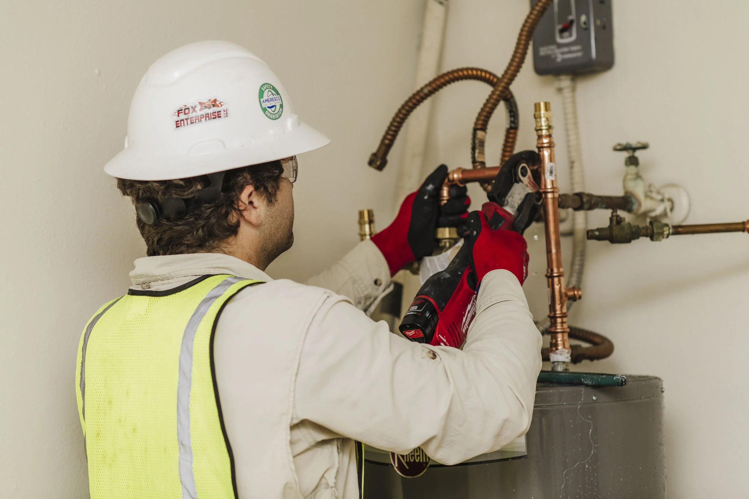 Plumber working on water heater, wearing hard hat and safety vest.