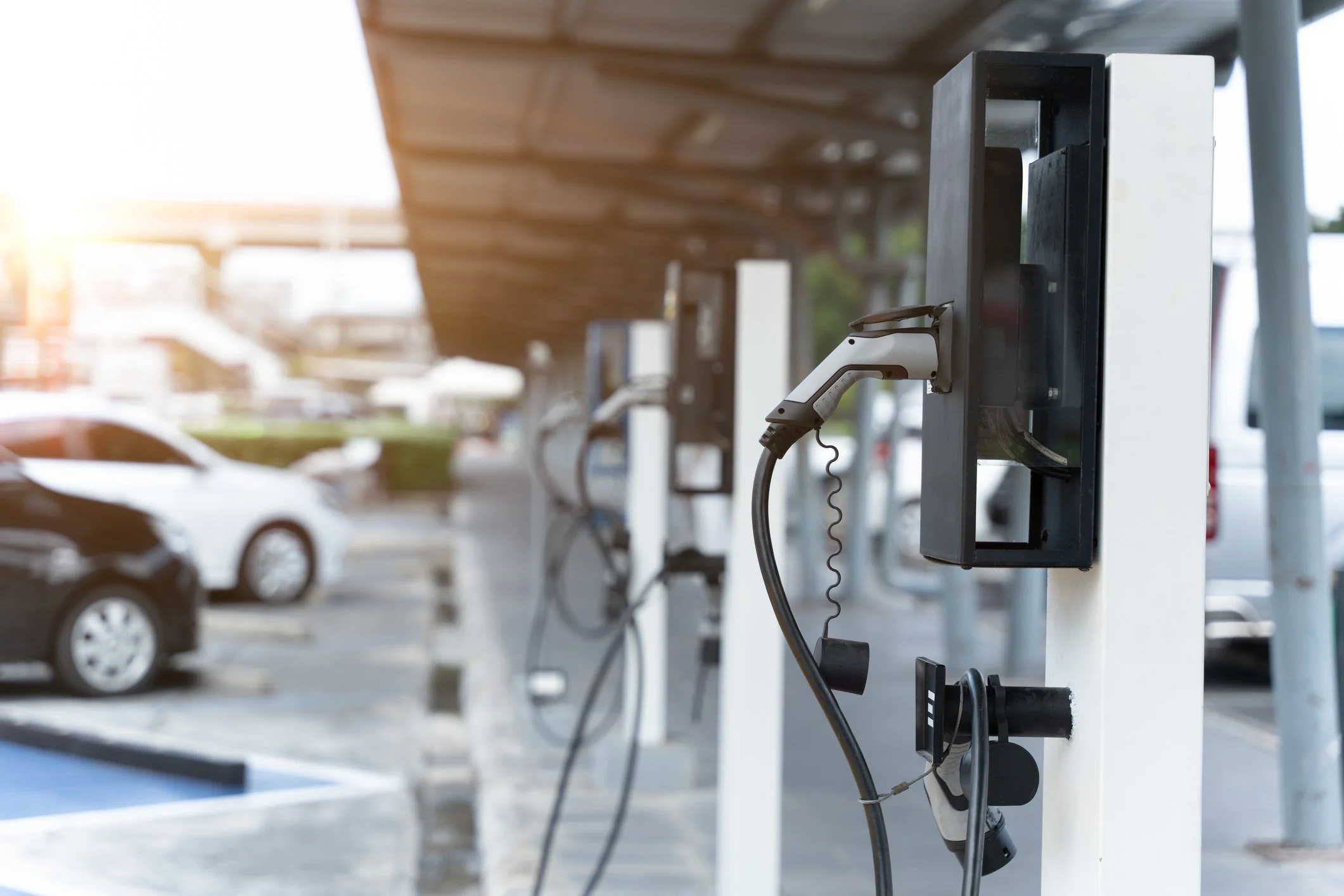 Electric vehicle charging stations in a parking lot with cars in the background.