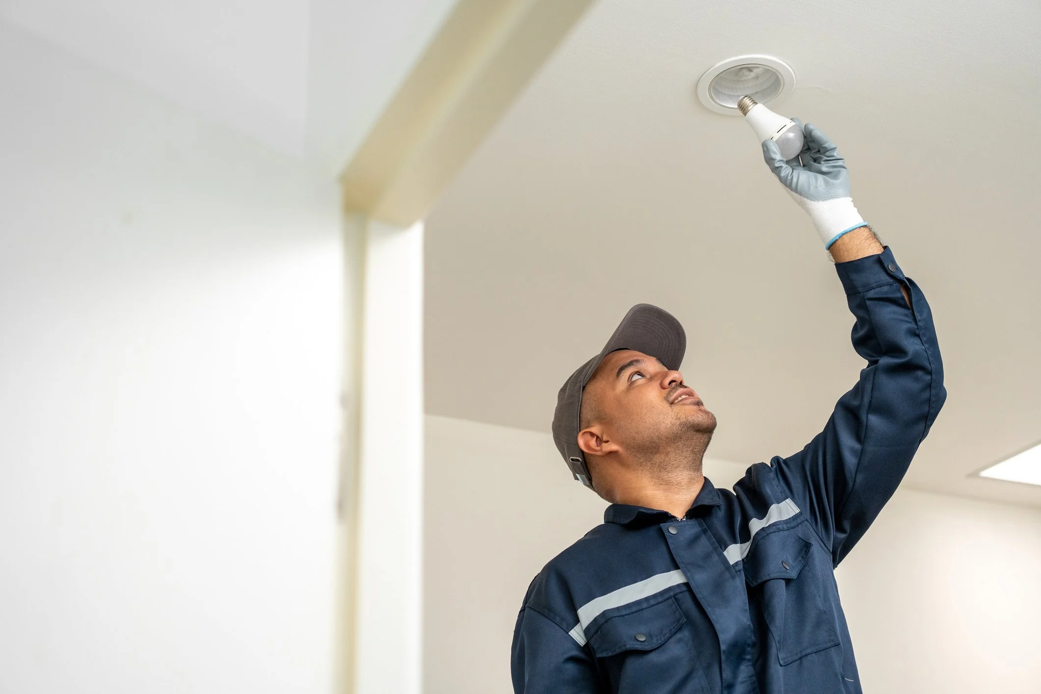 Electrician changing a ceiling light bulb indoors