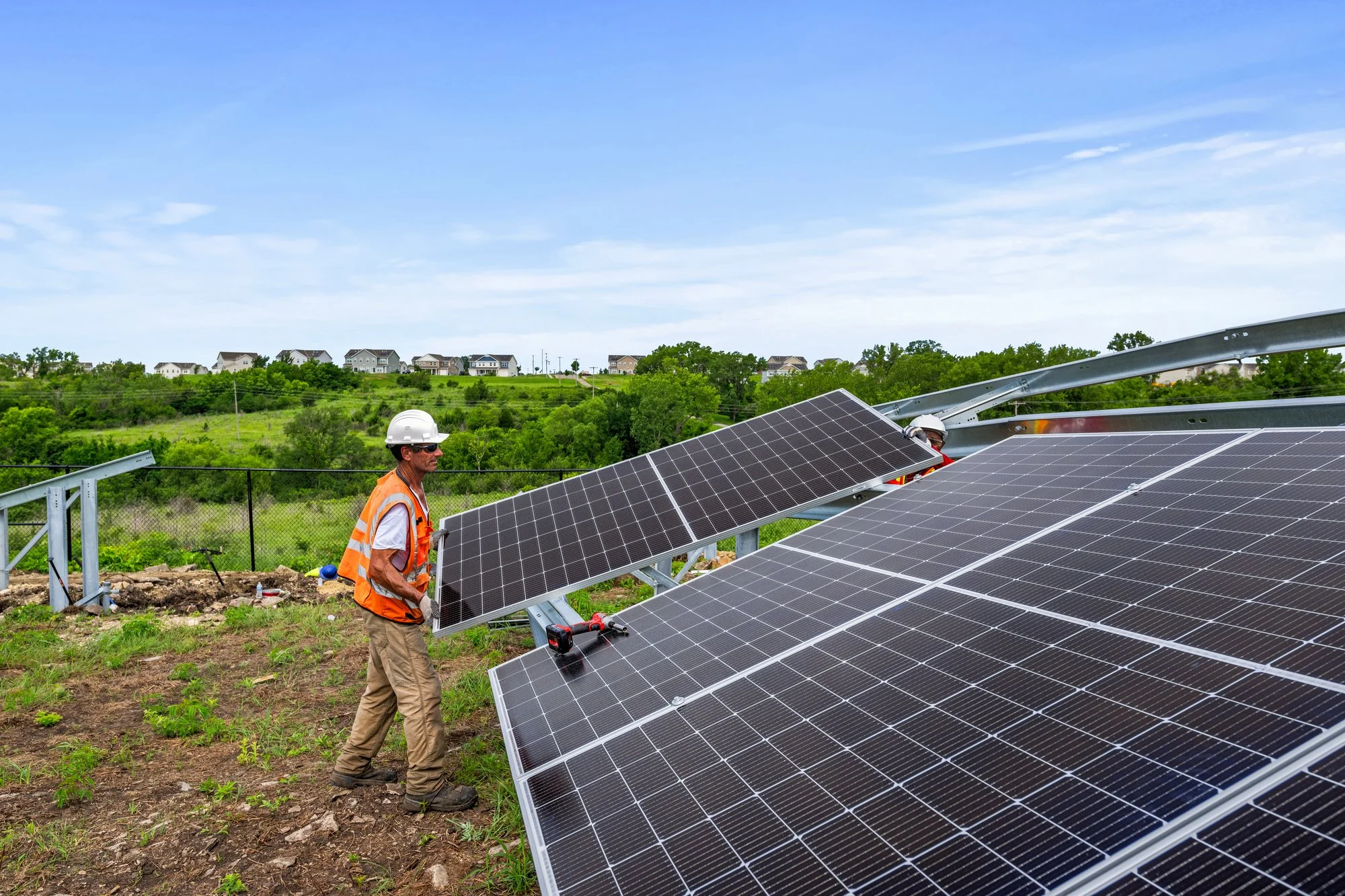 Workers installing solar panels on a grassy field under a blue sky.