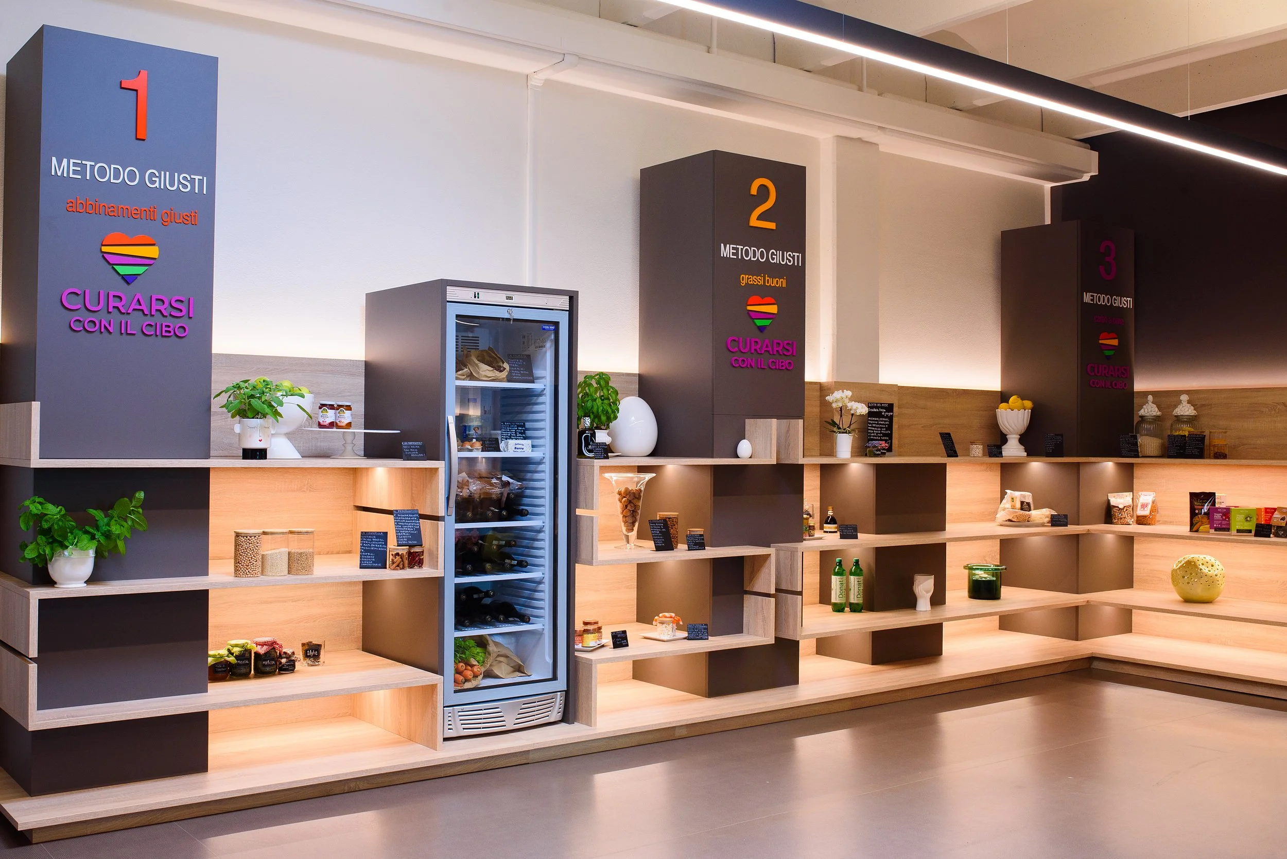 L'organizzazione di tre aree di rapido approvvigionamento alimentare con scaffali in legno e piante decorative, in un ambiente moderno e ben illuminato.