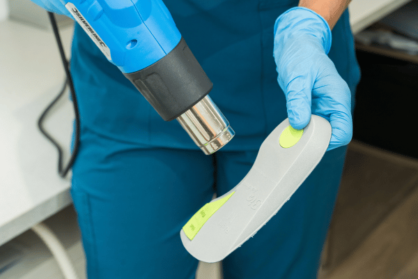 Image is of a podiatrist moulding orthotics with a heat gun at The Beale Clinic
