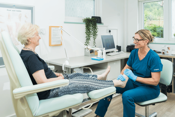 Image is of Clare Beale, Senior Podiatrist at The Beale Clinic, treating an elderly female patient and holding her foot