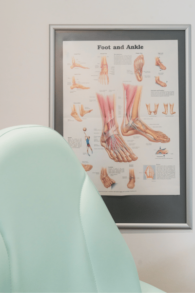 Image is of a podiatrists chair at The Beale Clinic with an anatomical poster of feet in the background