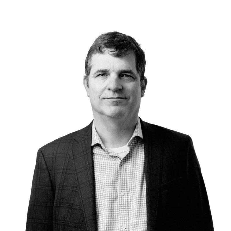 Black and white portrait of Charles Muggeridge in a checked shirt and dark blazer.