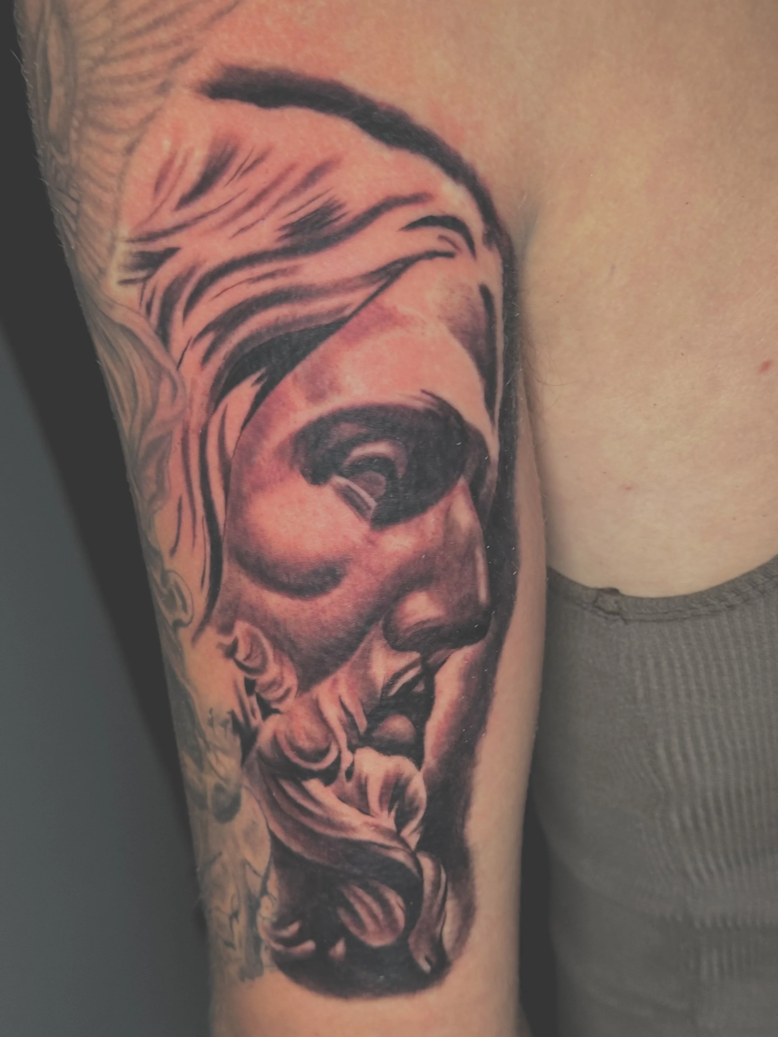 A detailed black and grey tattoo of Jesus' face on a person's upper arm.
