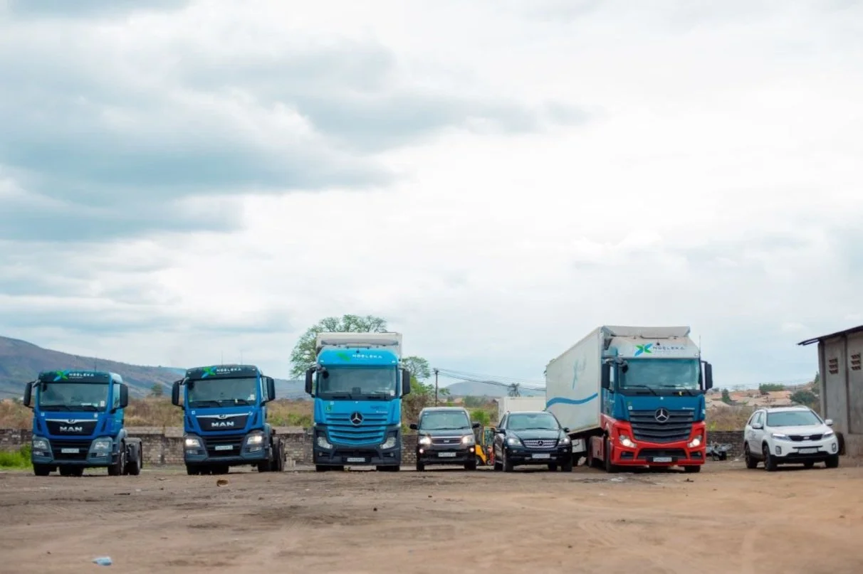 Plusieurs camions et voitures en stationnement dans un lieu en plein air avec un ciel nuageux.