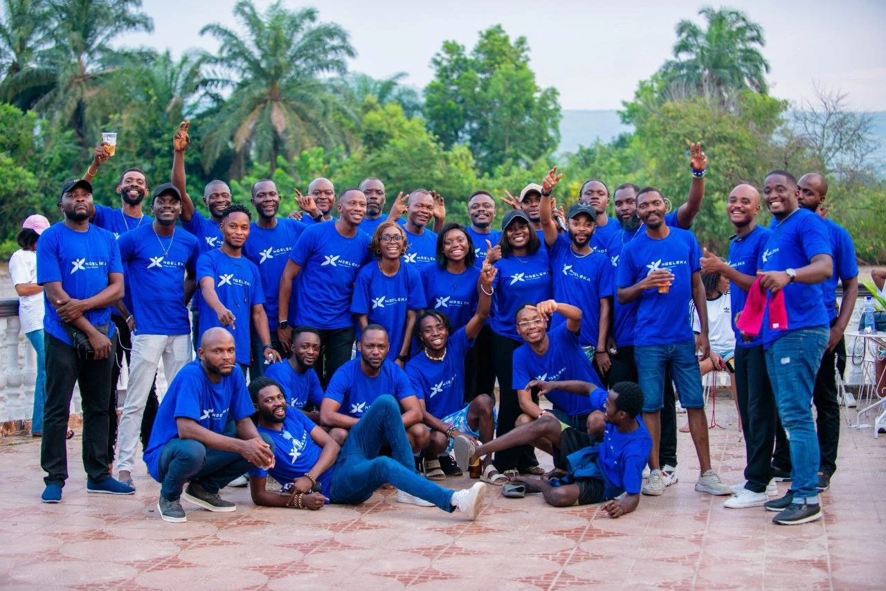 Groupe de personnes en t-shirts bleus, souriantes, posant pour une photo en plein air, avec une végétation luxuriante en fond.
