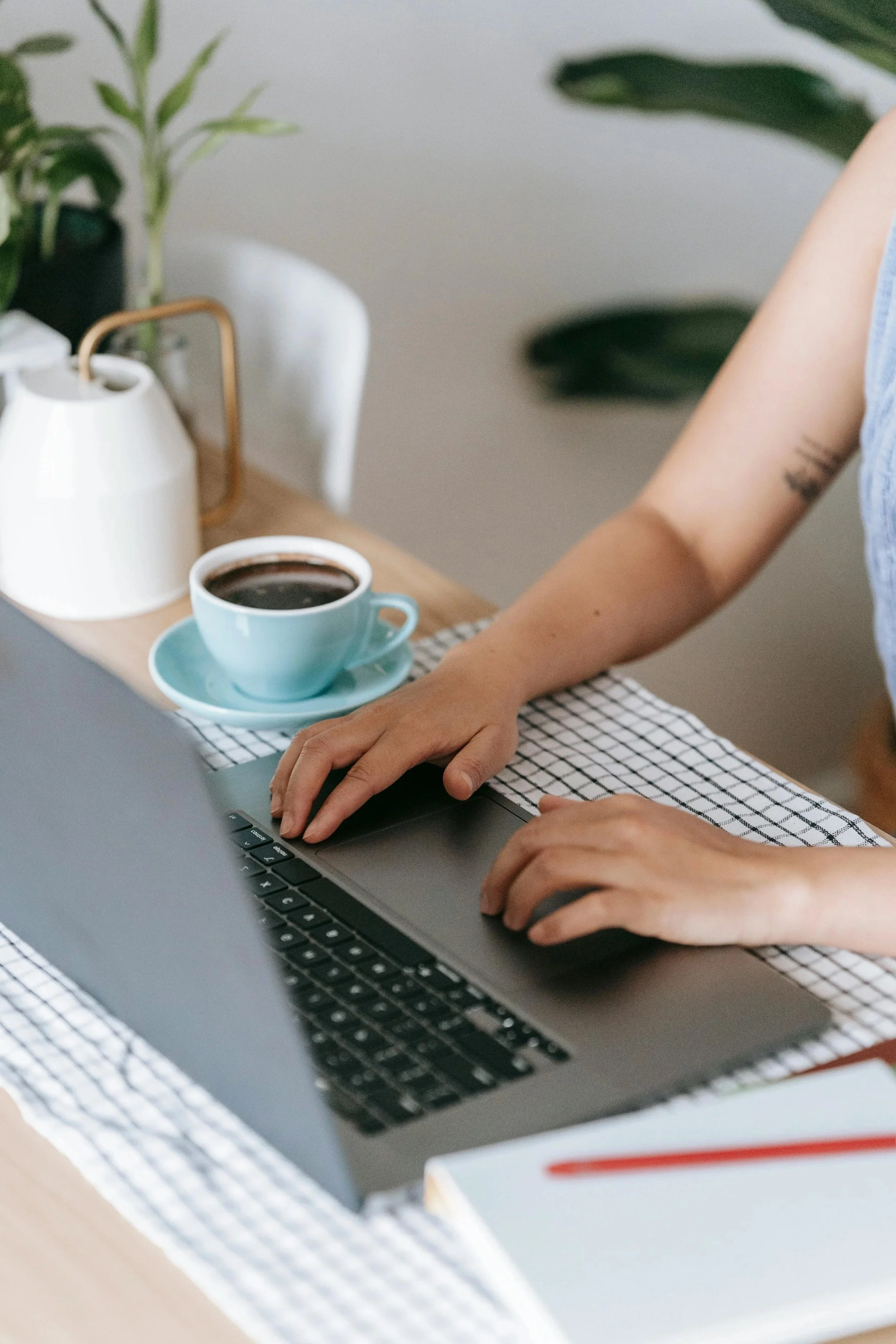 An image cropped in on a woman's hands typing a laptop with a cup of coffee next to her