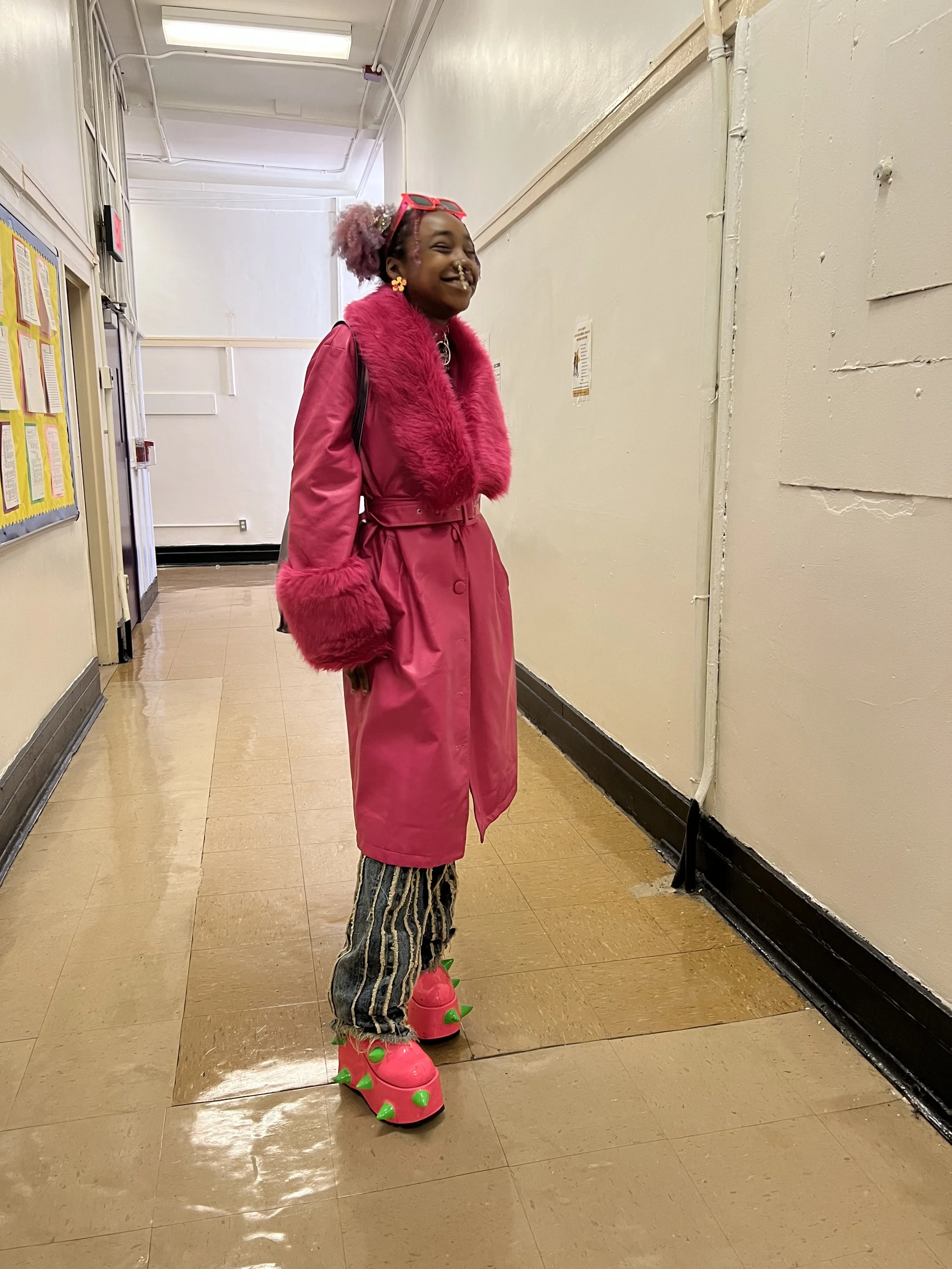  Smiling City-As-School studentin bright pink coat and shoes in hallway. 