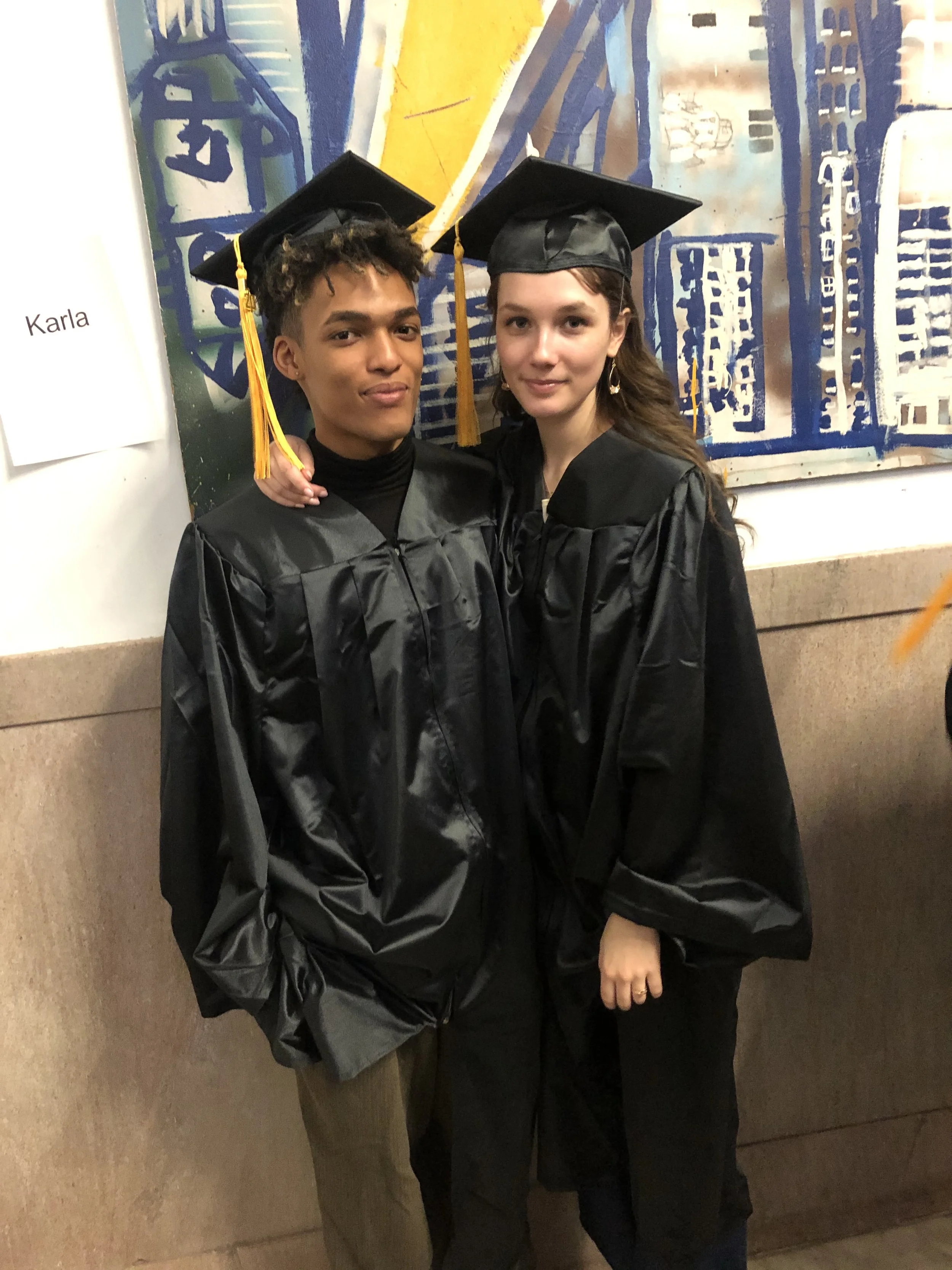  Two City-As-School students posing in graduation caps and gowns in school hallway. 