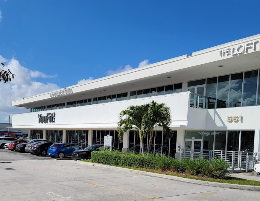 Modern shopping center with parked cars, palm trees, and the address number 561 on the building.