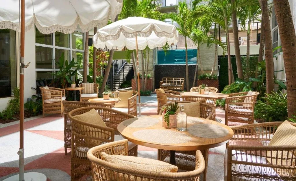 Outdoor patio area with round tables, wicker chairs, umbrellas, and lush green tropical plants.
