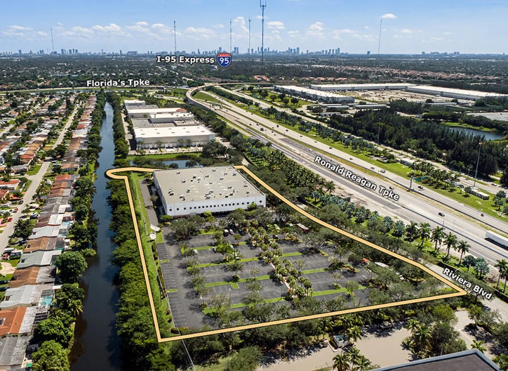 Aerial view showing a commercial area with a parking lot, a water canal, and nearby highways in a cityscape, with labels for I-95 Express, Florida's Turnpike, Ronald Reagan Turnpike, and Riviera Blvd.