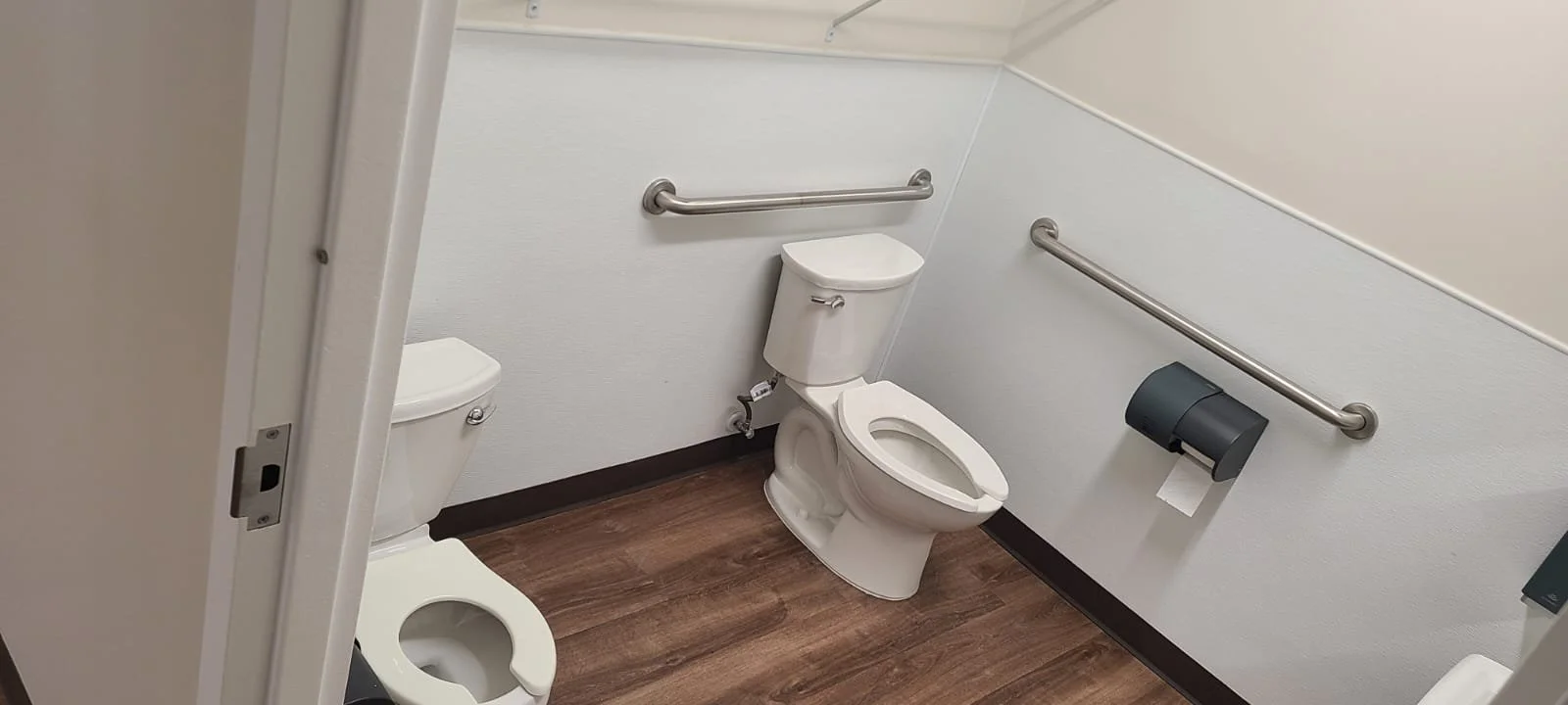 Accessible public restroom with a toilet, grab bars on the walls, and a toilet paper dispenser.