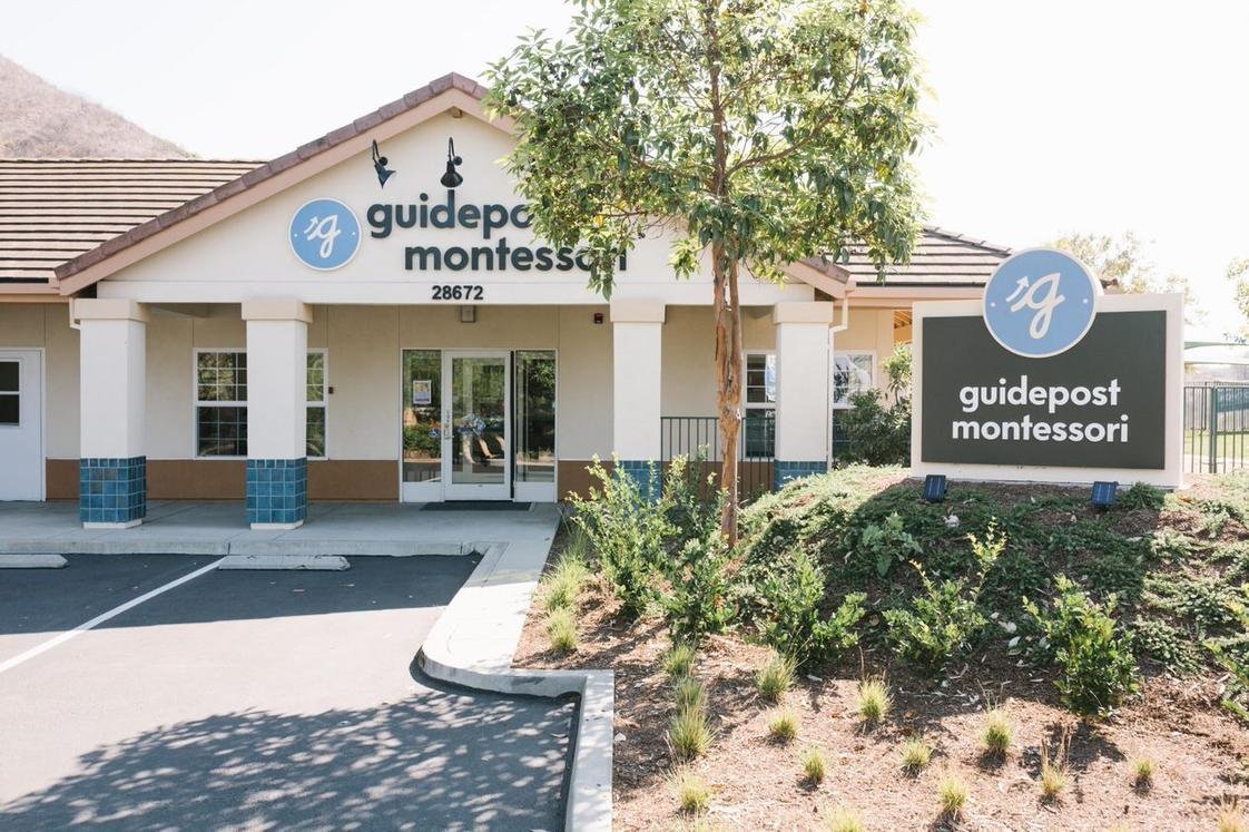 Exterior of a Guidepost Montessori school building with a sign, some trees, and landscaping in front.