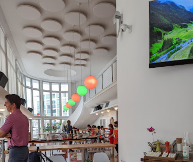 Interior of a modern cafe with hanging circular lights in red and green, large windows, and patrons ordering at the counter.