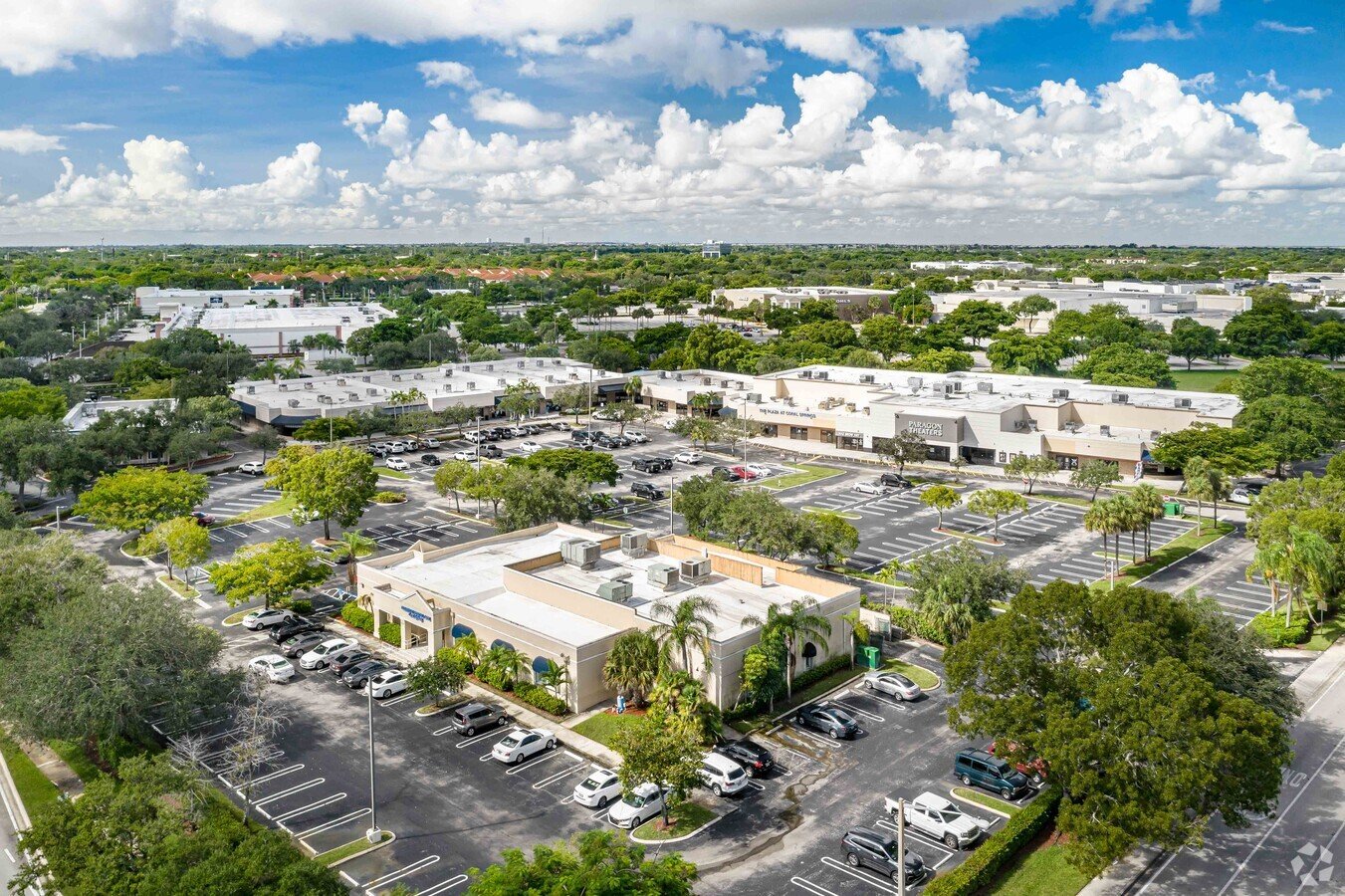 An aerial view of a commercial plaza with multiple buildings, parking lots, and green spaces, indicating a large-scale development.