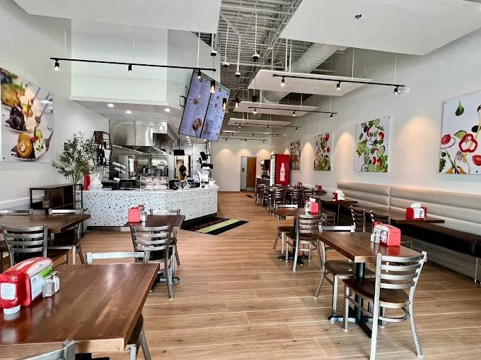 A brightly lit, modern restaurant interior with wooden tables and booths, suggesting a casual dining experience.