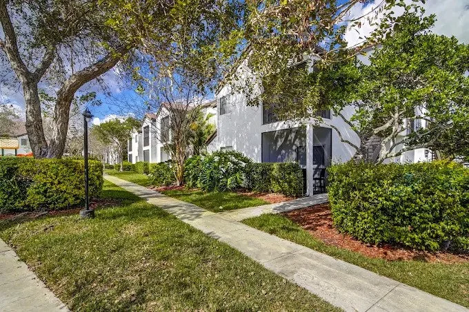 Apartment complex with well-maintained sidewalk, lush greenery, and trees.