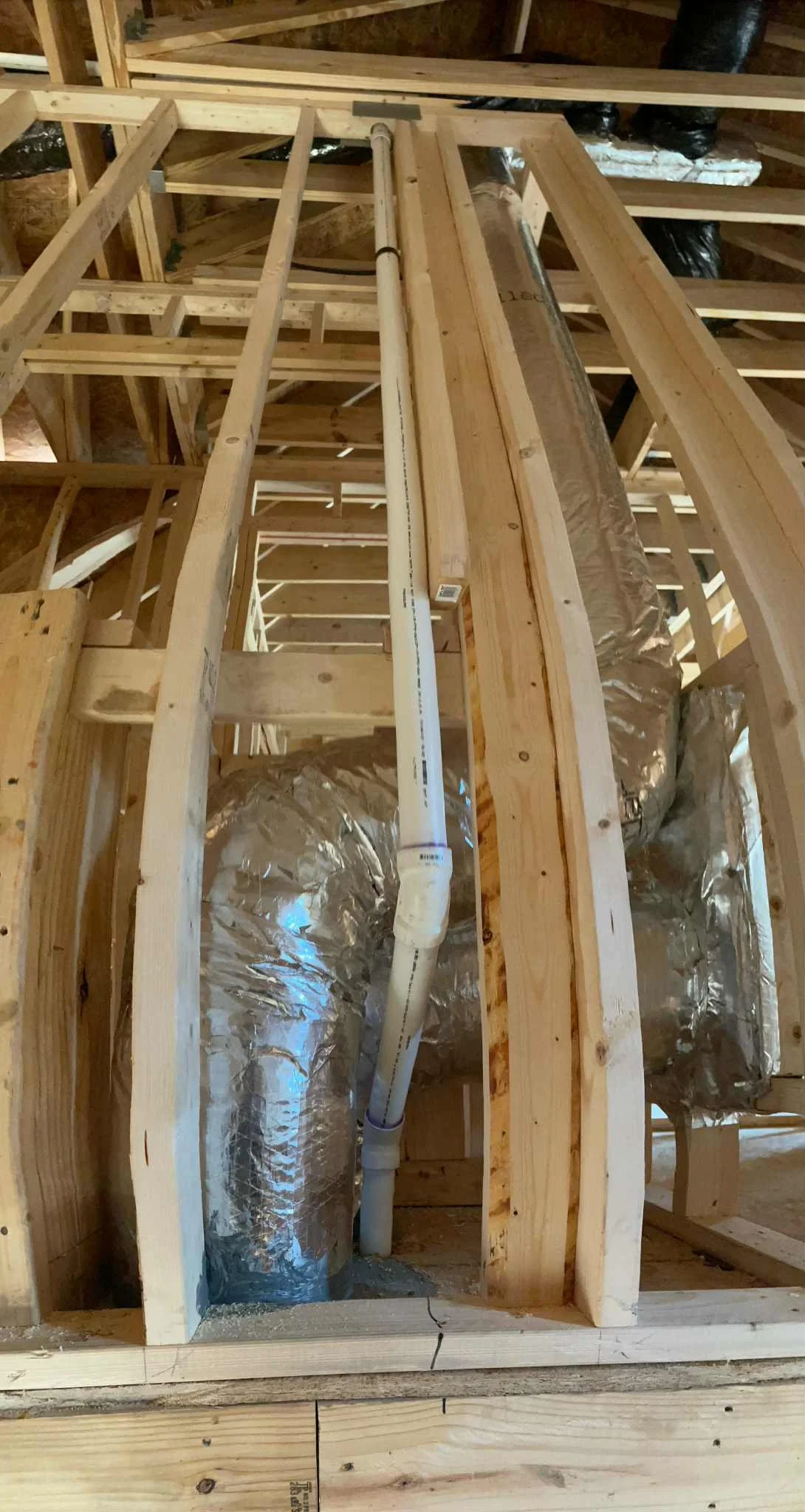 Construction framing with wooden studs and insulation duct work, showing plumbing pipes running vertically.