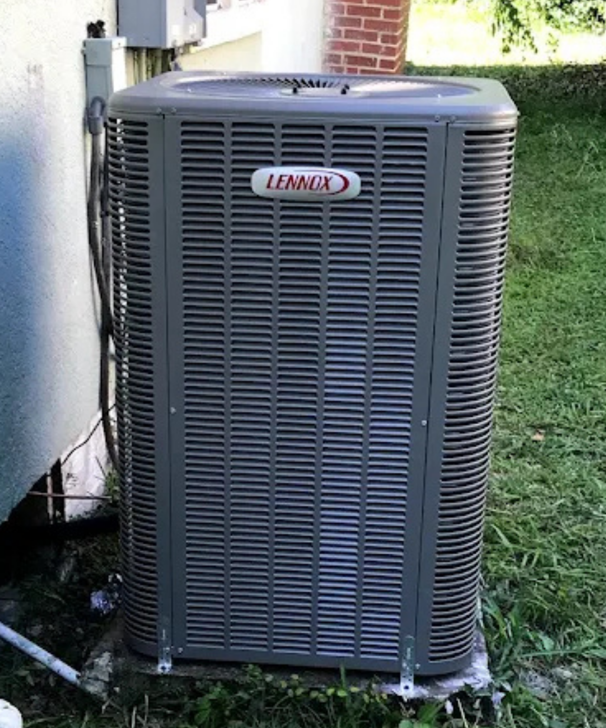 An outdoor Lennox air conditioning unit on a grassy area next to a wall.