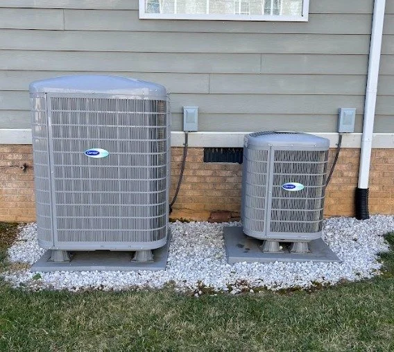 Two animal-shaped outdoor air conditioning units outside a house, set on gravel.
