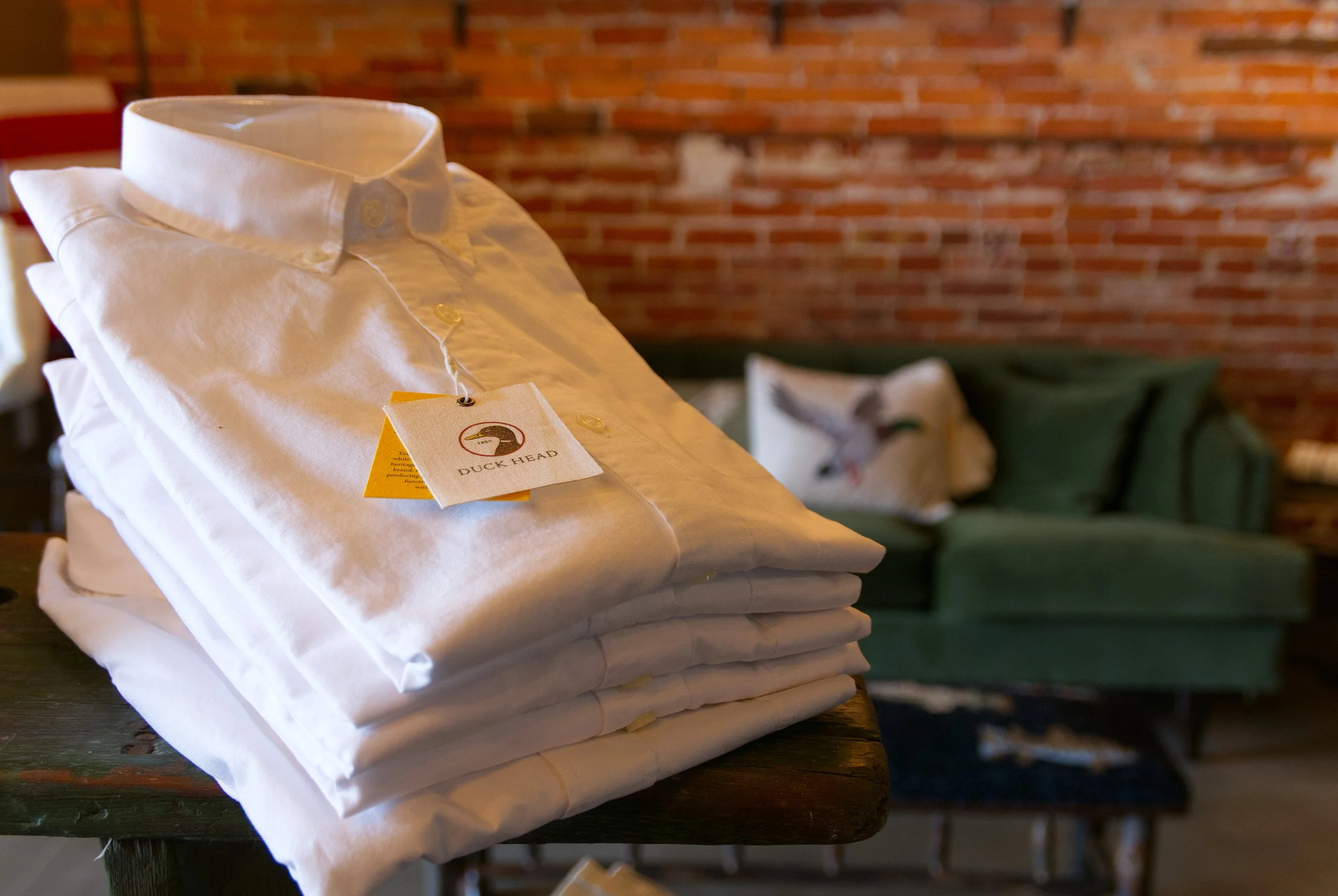 A stack of white oxford shirts from Duckhead in a cozy brick-walled showroom 