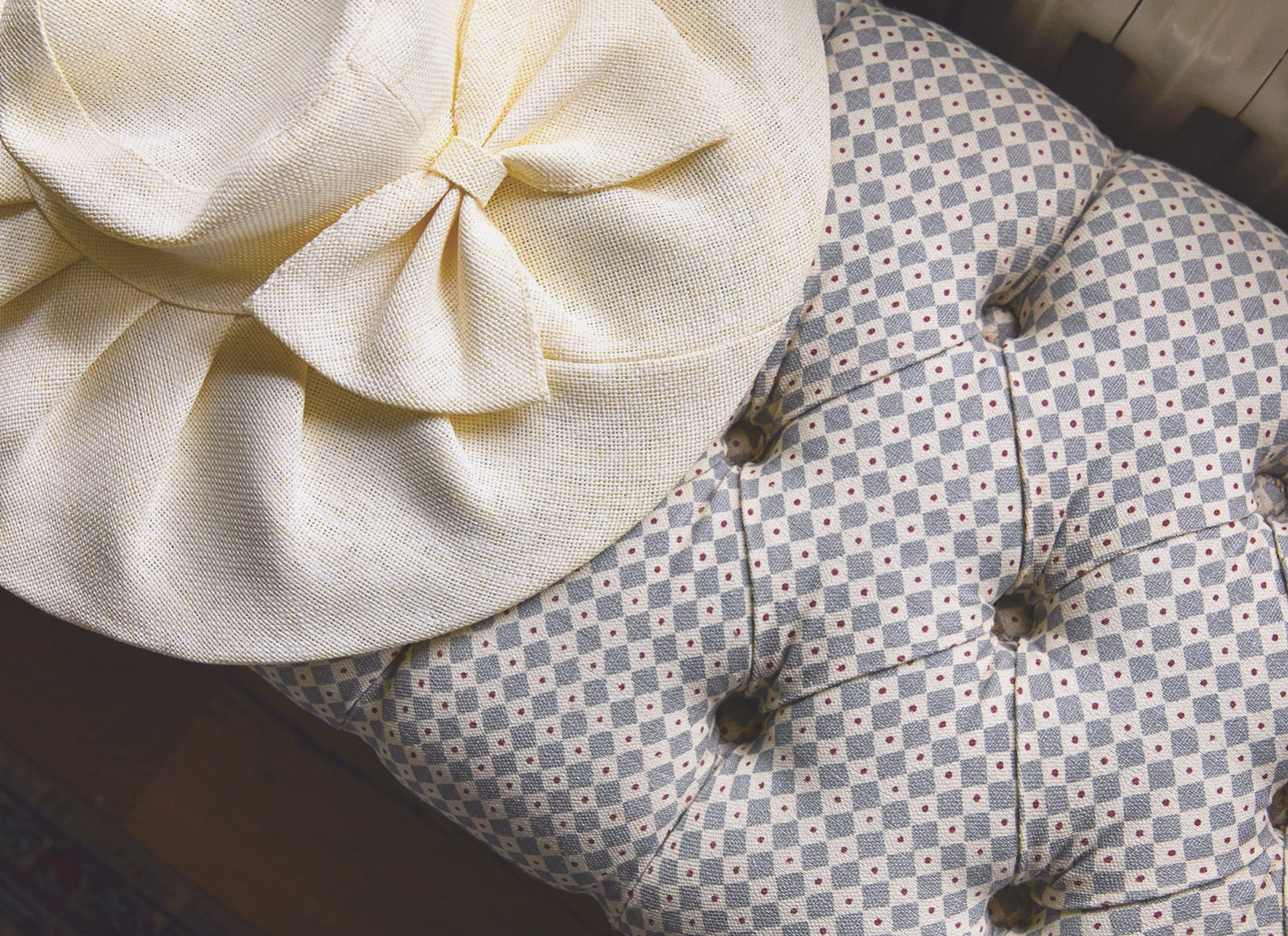 Close-up of a beige fabric hat with a bow resting on a padded armchair with a blue and white checkered pattern.