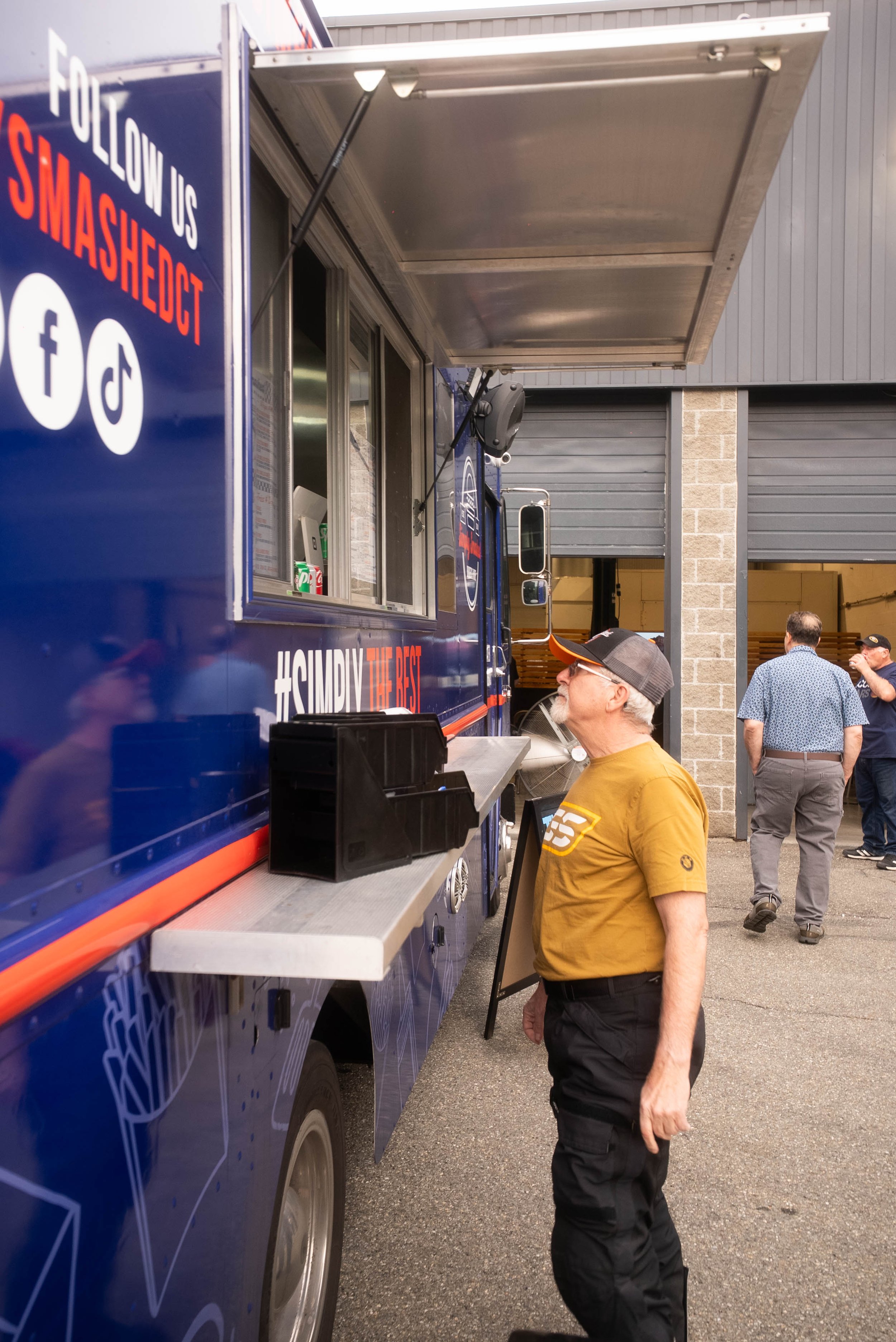 Man ordering at a food truck with social media logos and hashtag "#SimplyTheBest" on the side.