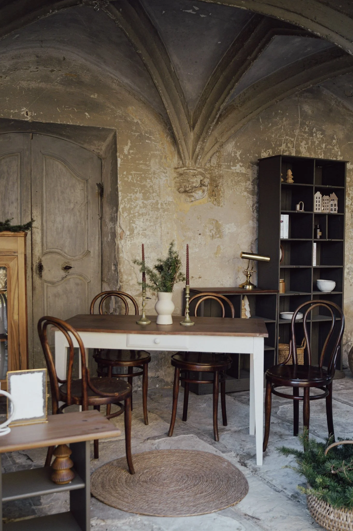 Intérieur de salle à manger rustique avec table, chaises en bois, étagère noire, décorations de Noël et murs en pierre et plâtre ancien.