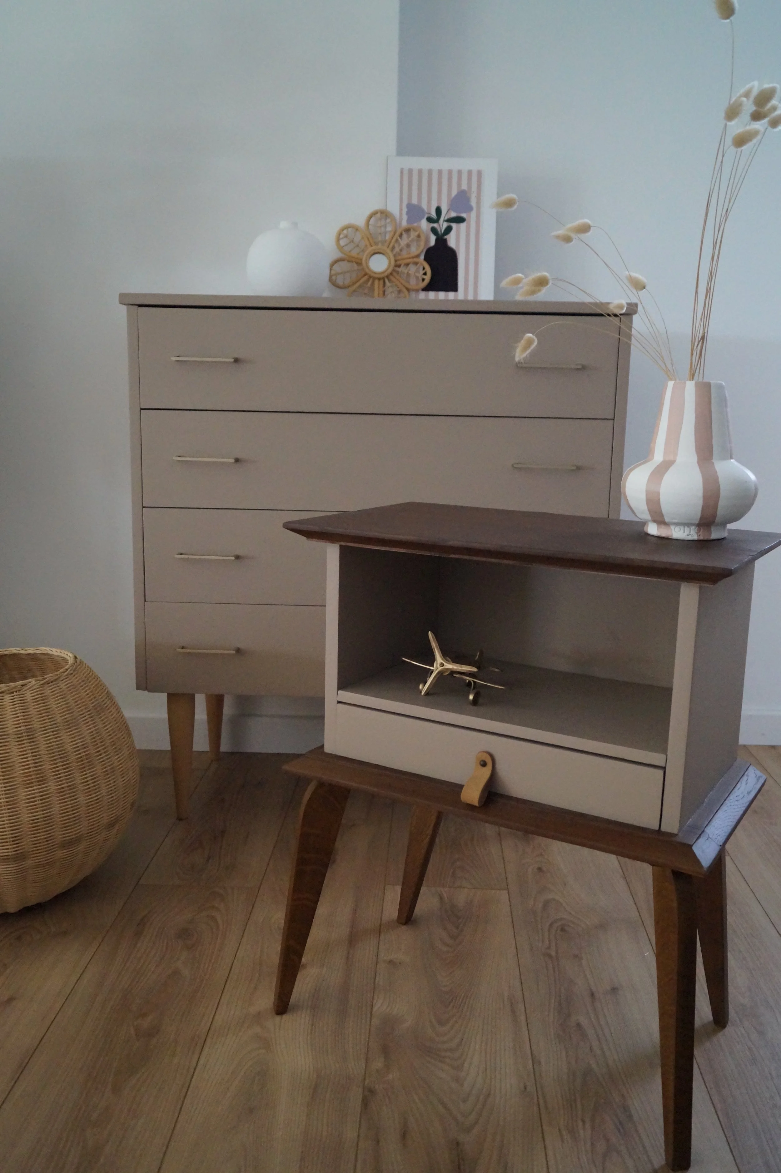 Une pièce avec une commode beige, une petite table en bois, un vase avec des branches de pampa, une décoration sur la commode, et un panier en rotin