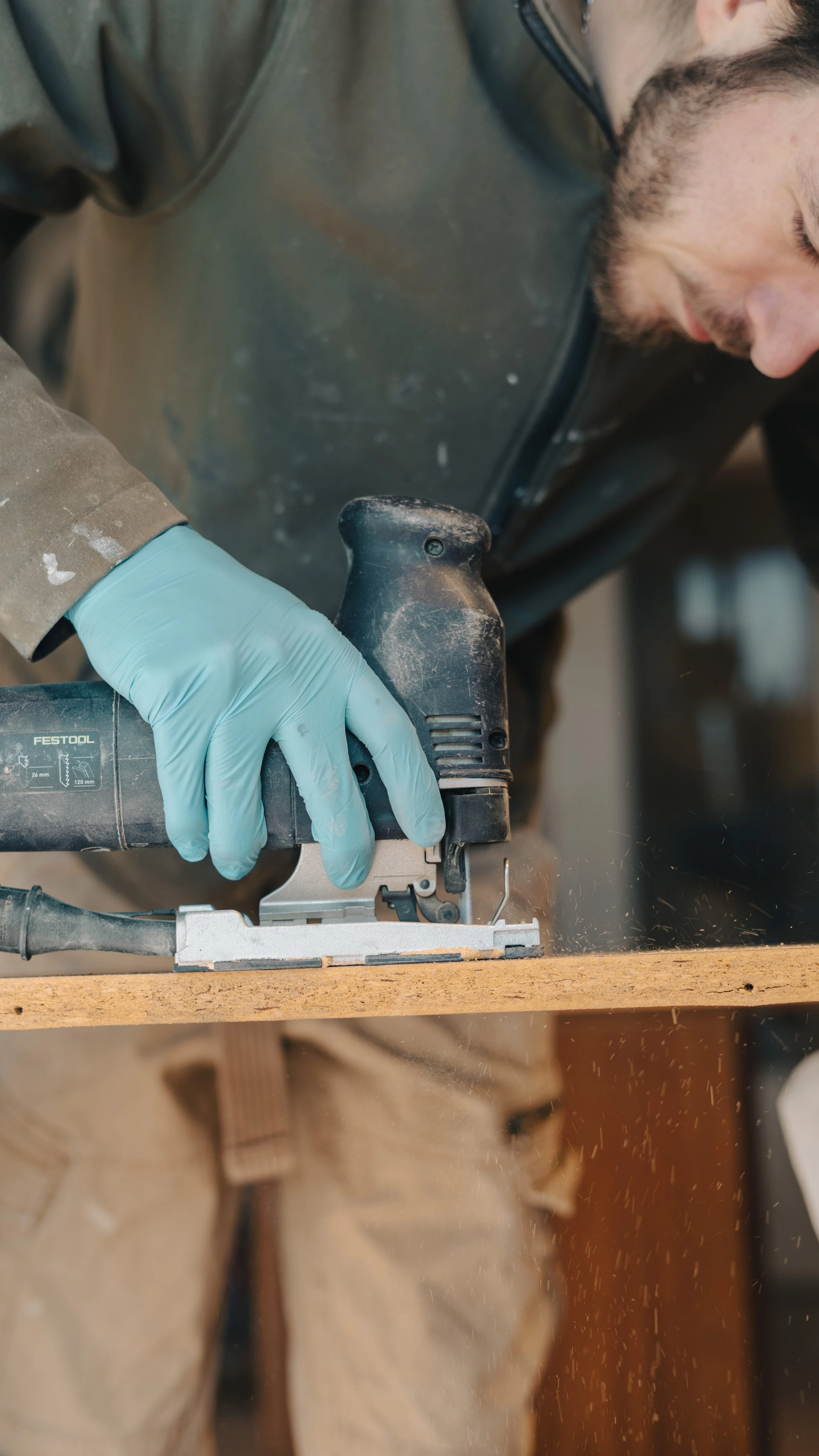 Un homme portant des gants en latex travaille avec une scie électrique sur une pièce de bois.