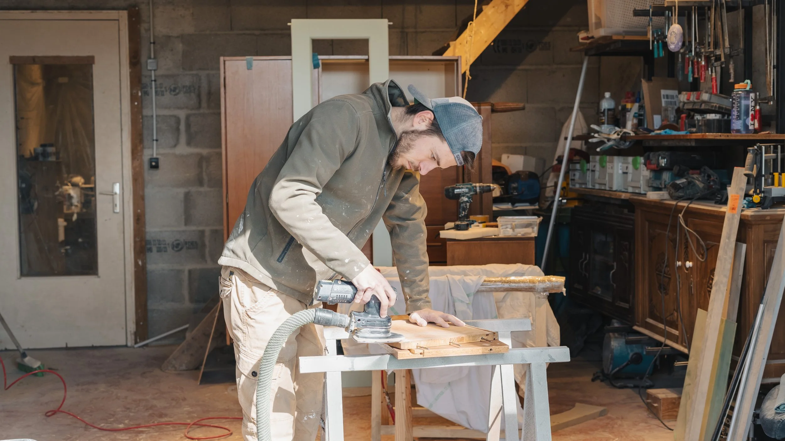 Un homme travaillant dans un atelier de bricolage, utilisant une ponceuse sur un morceau de bois placé sur une table.